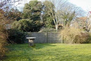 A backyard with a wooden fence, a stone table, and various trees and shrubs. - Holiday apartment with 2 bedrooms (Borkum)