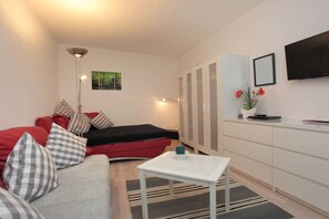 Ein gemütlicher Wohnbereich mit Sofa, kleinem Tisch, Schrank und Fernseher.