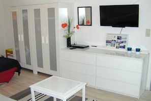 A room with a white wardrobe, a flat-screen TV mounted on the wall, a small table, and a vase with flowers. - Holiday apartment with 2 bedrooms (Borkum)