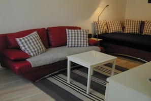 A living room with a red sofa, a white coffee table, and a black sofa with checkered cushions. - Holiday apartment with 2 bedrooms (Borkum)