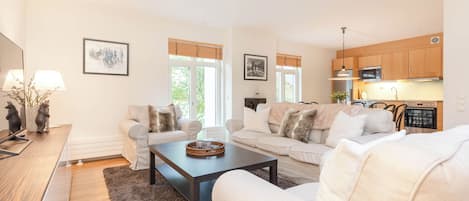 Una sala de estar moderna con sofá, mesa de centro y una zona de cocina con armarios de madera y electrodomésticos.