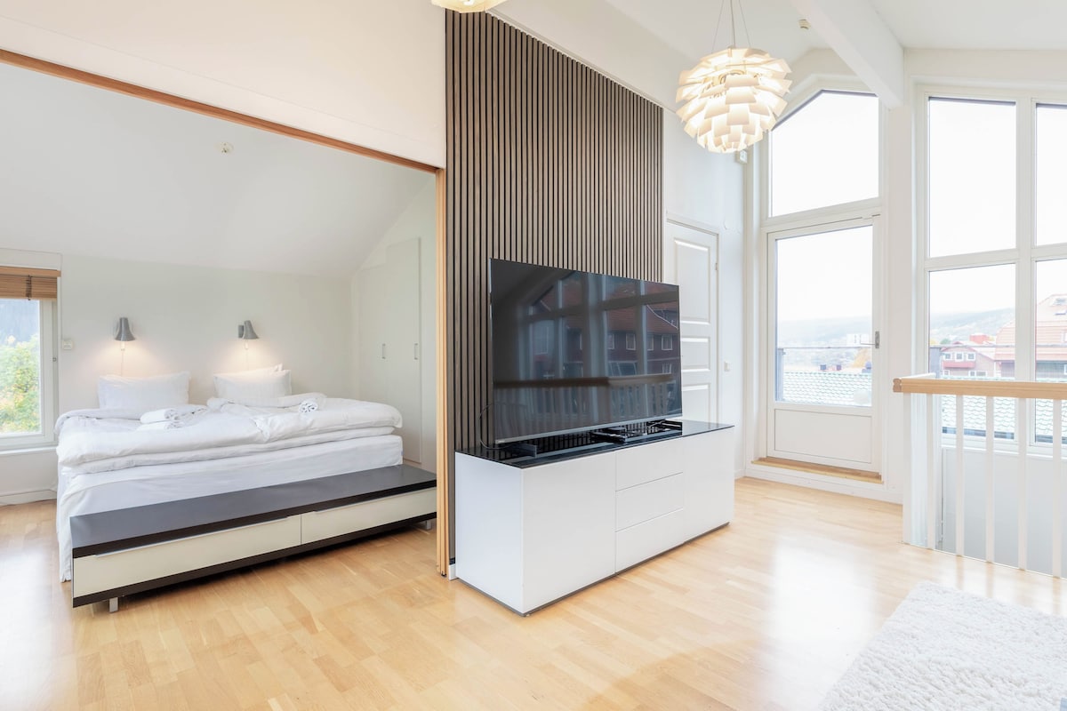 Ein modernes Schlafzimmer mit einem Bett, einem an der Wand montierten Fernseher und einem großen Fenster.