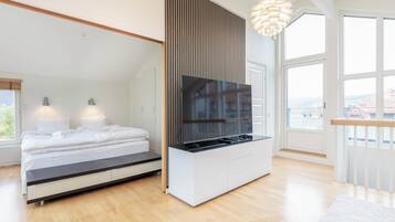 A modern bedroom with a bed, a TV mounted on a wall, and a large window.