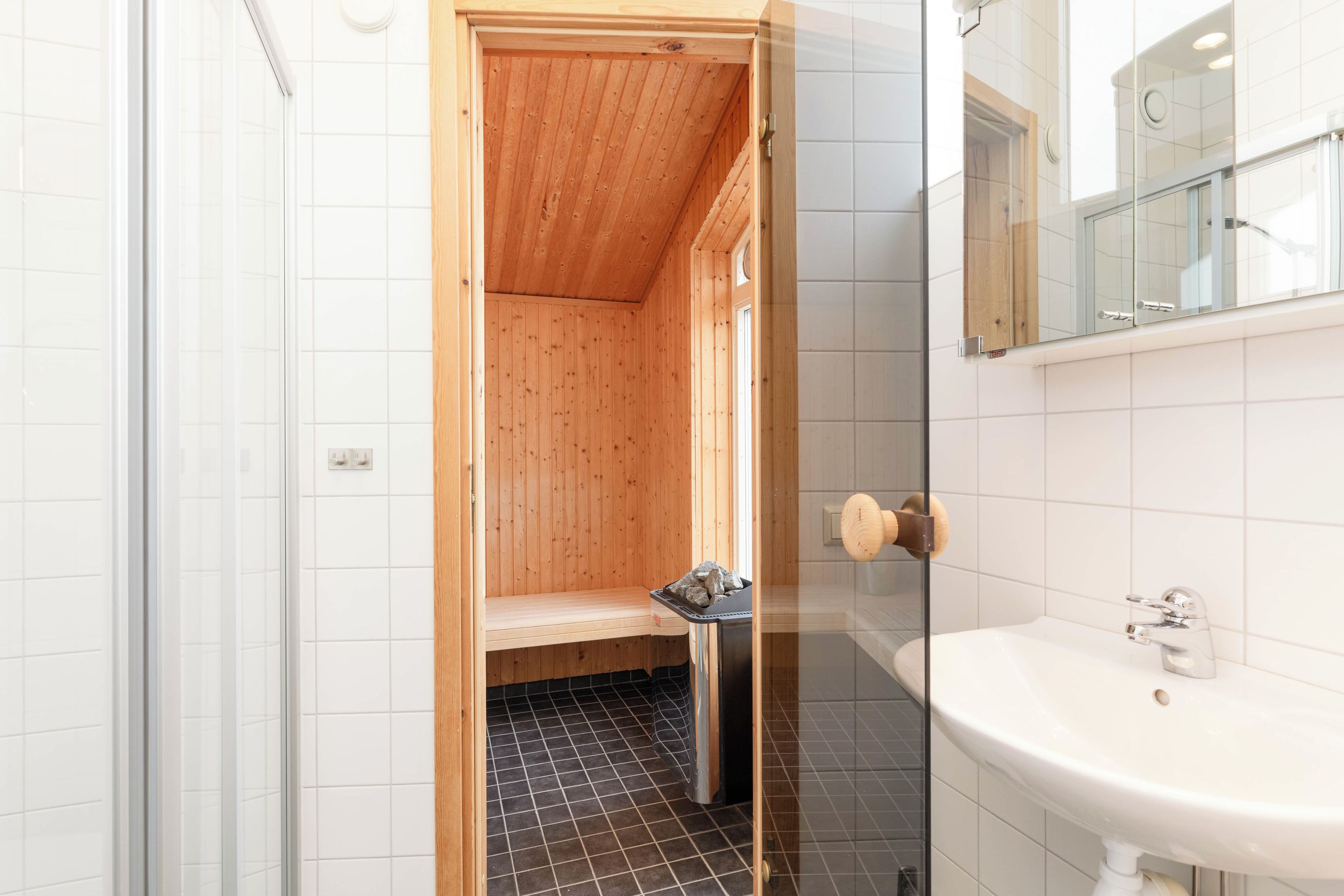A small, compact bathroom with a wooden shower enclosure, a sink, and a mirror.