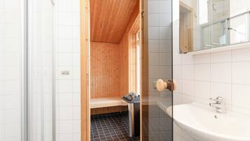 A small, compact bathroom with a wooden shower enclosure, a sink, and a mirror.