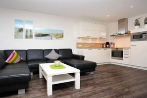 A modern living area with a black leather sofa, a white coffee table, and a kitchen with white cabinets and a microwave. - Holiday apartment with 2 bedrooms (Borkum)