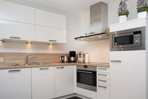 A modern kitchen with white cabinetry, a built-in oven, a microwave, and a coffee maker. - Holiday apartment with 2 bedrooms (Borkum)