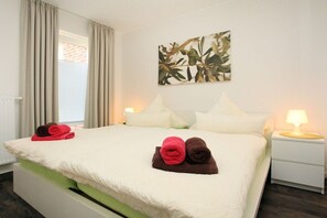 A hotel room with a bed, pillows, a nightstand, a lamp, and a wall art piece. - Holiday apartment with 2 bedrooms (Borkum)