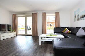 A modern living room with a black leather sofa, a white coffee table, and a flat-screen TV on a white cabinet. - Holiday apartment with 2 bedrooms (Borkum)