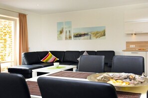 A modern living room with a black leather sofa, a dining table with chairs, and a kitchen area with a white cabinet. - Holiday apartment with 2 bedrooms (Borkum)