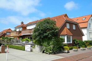 Een woonstraat met huizen, een verharde stoep en een boom.