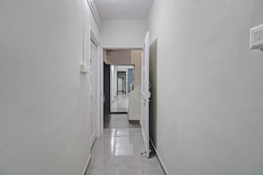 A narrow, well-lit hallway with white walls and a shiny floor, leading to a door at the end. - Hotel O Moonlight Inn (Nagpur)