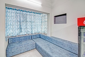 A room with a blue sectional sofa, a window with patterned curtains, a small wall-mounted TV, and a vending machine. - Hotel O Moonlight Inn (Nagpur)