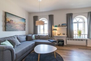 Een moderne woonkamer met een grijze hoekbank, een ronde salontafel en een schilderij aan de muur.