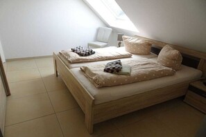 A bedroom with a wooden bed, two pillows, a chair, and a small table. - Holiday apartment with 2 bedrooms (Borkum)