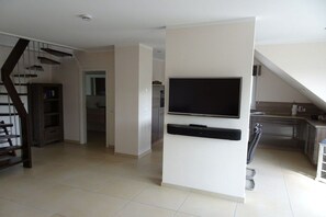 A modern living space with a flat-screen TV mounted on a white wall, a kitchen area with stainless steel appliances, and a staircase leading to another level. - Holiday apartment with 2 bedrooms (Borkum)