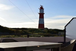 A red and white lighthouse on a hill, a table, and wicker chairs on a balcony. - Holiday apartment with 2 bedrooms (Borkum)