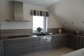 A modern kitchen with a built-in stove, a window with a striped valance, and a sink. - Holiday apartment with 2 bedrooms (Borkum)
