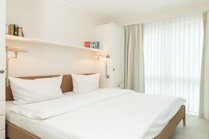 A hotel room with a bed, a nightstand, a lamp, a wardrobe, and a window with curtains. - Holiday apartment in Juist with sauna (Juist)