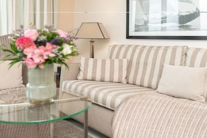 Ett vardagsrum med en randig soffa, ett soffbord i glas och en vas med blommor.