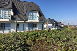 A two-story house with a dark roof, multiple windows, and a flag on the right. - Holiday apartment with 3 bedrooms (Hörnum)