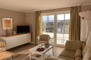 A living room with a sofa, a coffee table, a television on a cabinet, and a sliding glass door leading to a balcony. - Holiday apartment with 3 bedrooms (Hörnum)