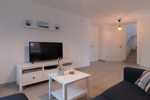 A modern living room with a flat-screen TV, a white coffee table, and a sofa. There is a staircase leading to another level. - Holiday apartment with 2 bedrooms (Krummhörn)