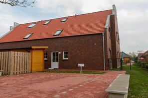A brick building with a red-tiled roof, a wooden fence, and a paved driveway. - Holiday apartment with 2 bedrooms (Krummhörn)