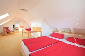 A modern bedroom with a sloped ceiling, a bed with red bedding, a wooden chair, and a desk with a lamp. - Seestern No. 2 Apartment House Seestern (Norderney)