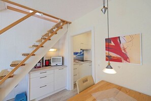 A compact kitchen with a wooden staircase, a dining area with a table, and a wall-mounted artwork. - Seestern No. 2 Apartment House Seestern (Norderney)