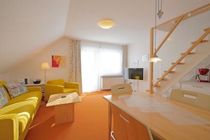 A room with a yellow sofa, a wooden desk, a television, and a staircase. - Seestern No. 2 Apartment House Seestern (Norderney)