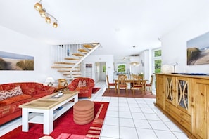 A spacious living area with a staircase, a dining set, and a large window. - Holiday home in Dornum with Wi-Fi and gym (Dornum)
