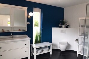 A bathroom with a white vanity, a large mirror, a white toilet, and a white shelf with towels. - Holiday home in Tossens with swimming pool (Tossens)