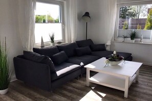 A modern living room with a dark sofa, a white coffee table, and a floor lamp. - Holiday home in Tossens with swimming pool (Tossens)