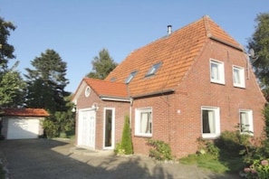 A two-story brick house with a sloped roof, a garage, and a small garden area. - Holiday home in Tossens with swimming pool (Tossens)