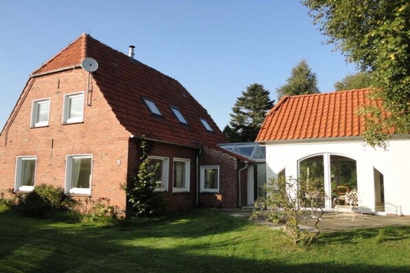 A two-story house with a red-tiled roof, a brick exterior, and a white exterior wall with a glass door. - Holiday home in Tossens with swimming pool (Tossens)