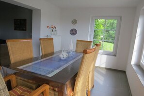 A dining area with a wooden table, wicker chairs, and a view of greenery outside. - Holiday apartment with 1 bedroom (Dornum)
