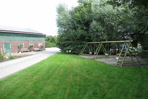 A grassy area with a swing set and a brick building with a green roof. - Holiday apartment with 1 bedroom (Dornum)