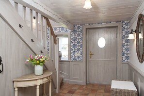 En hall med en trätrappa, en dörr med ett runt fönster och en vägg med blått blommönstrat tapet.