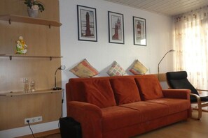 A living room with a sofa, a black chair, and a wooden shelf with decorative items. - Neptune House Iderhoff Norderney (Norderney)