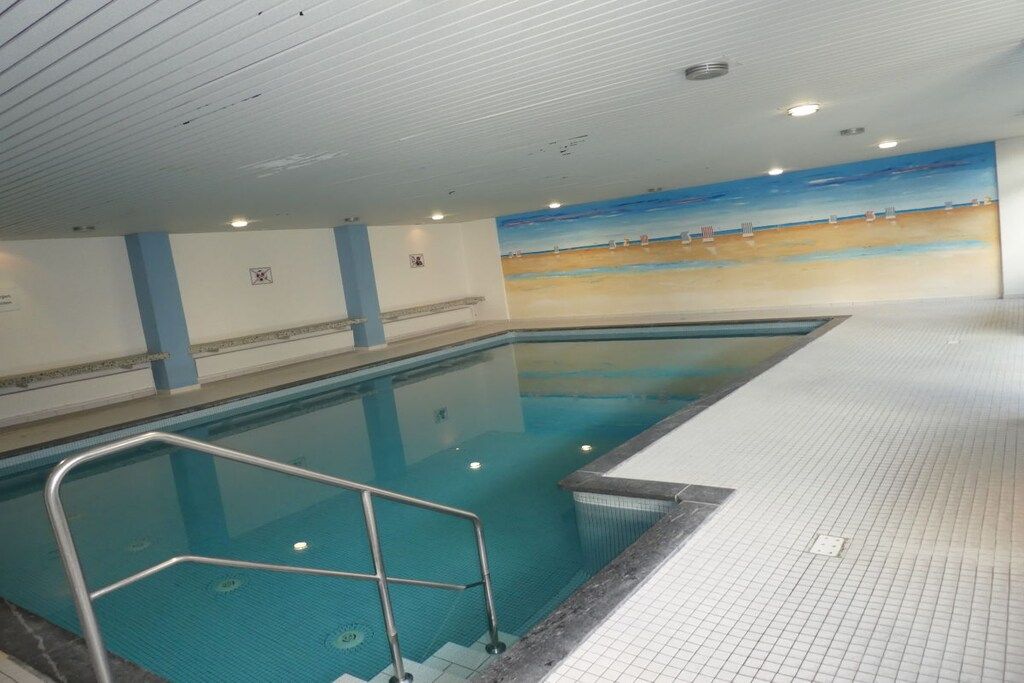 Une piscine intérieure avec un sol carrelé et une fresque murale représentant une scène de plage.