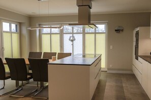 Eine moderne Küche mit einer Kochinsel, einem Essbereich mit Stühlen und großen Fenstern mit Jalousien.