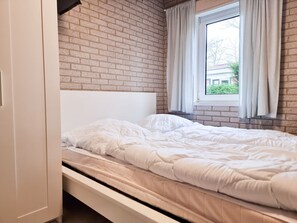 A single bed with a headboard, a window with curtains, and a brick wall. - Zo03 Holiday Home/apartment With pet (Zoutelande)