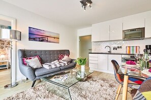 A modern living room with a grey sofa, a glass coffee table, and a dining area with colorful chairs and a glass table. - Holiday apartment in Hörnum with Wi-Fi (Hörnum)