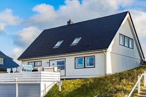Een huis met twee verdiepingen, een donker dak, meerdere ramen en een witte gevel.