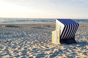 A beach with a striped beach chair and a wooden structure, possibly a lifeguard stand, in the foreground. - Holiday apartment with 1 bedroom (Norderney)