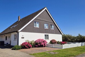 A two-story house with a gabled roof, white exterior walls, and a small porch. - Holiday apartment with 1 bedroom (Norderney)