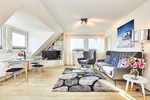 A modern living room with a sofa, armchairs, a coffee table, and a dining area with chairs and a glass table. - Holiday apartment in Hörnum with Wi-Fi (Hörnum)