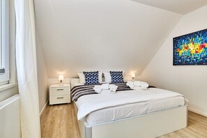 A bedroom with a bed, bedside tables, a nightstand, a painting, and a window with curtains. - Holiday apartment in Hörnum with Wi-Fi (Hörnum)