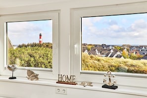 A window with two views: one of a lighthouse and one of a residential area with houses and greenery. - Holiday apartment in Hörnum with Wi-Fi (Hörnum)